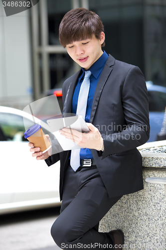 Image of Young Asian business executive in suit holding tablet and coffee