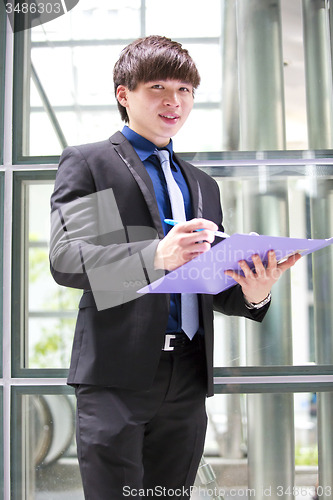 Image of Young Asian business executive in suit holding file