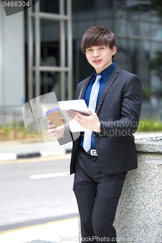 Image of Young Asian business executive in suit holding tablet and coffee