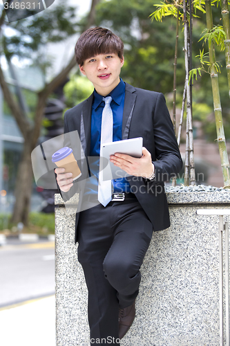 Image of Young Asian business executive in suit holding tablet and coffee