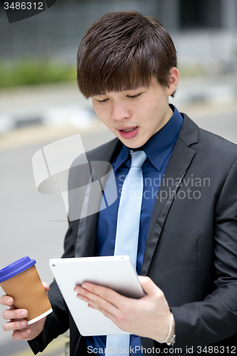 Image of Young Asian business executive in suit holding tablet and coffee