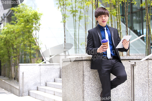 Image of Young Asian business executive in suit holding tablet and coffee