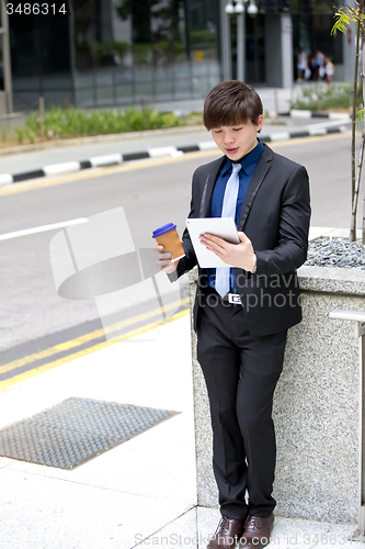 Image of Young Asian business executive in suit holding tablet and coffee