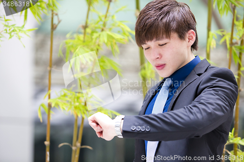 Image of Young Asian business executive in suit looking at time