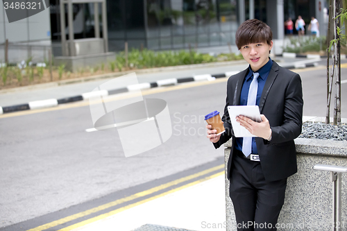Image of Young Asian business executive in suit holding tablet and coffee