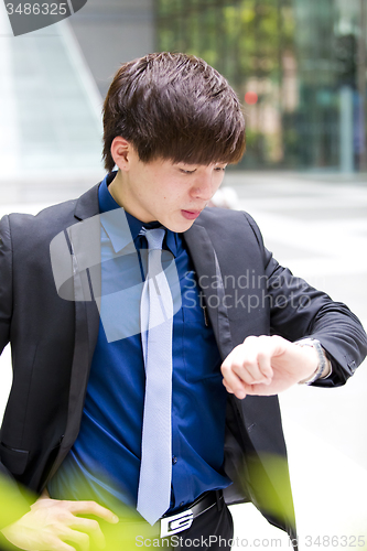 Image of Young Asian business executive in suit looking at time