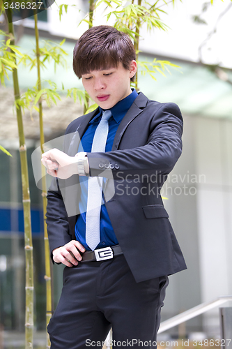 Image of Young Asian business executive in suit looking at time