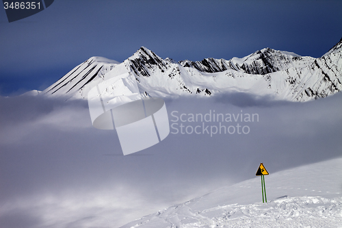 Image of Warning sing on ski slope and mountains in fog