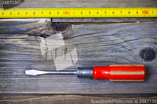 Image of old screwdriver, three screws and measuring tape on textured boa