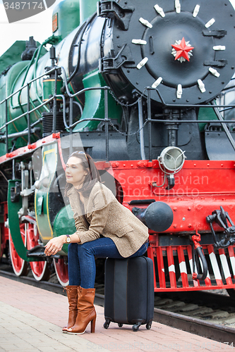 Image of pretty woman sitting on a suitcase on railroad station
