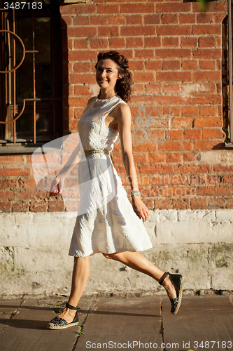 Image of pretty tanned middle-aged woman in a white dress