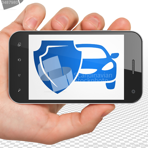 Image of Insurance concept: Hand Holding Smartphone with Car And Shield on display