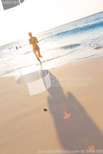 Image of Woman running on the beach in sunset.