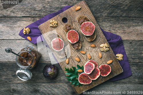Image of Sliced figs, nuts and bread with jam on wooden choppingboard