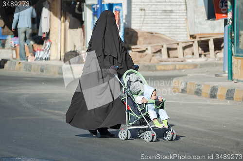 Image of Arabic woman in hijab conducts carriage with child