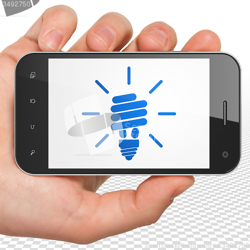 Image of Business concept: Hand Holding Smartphone with Energy Saving Lamp on display