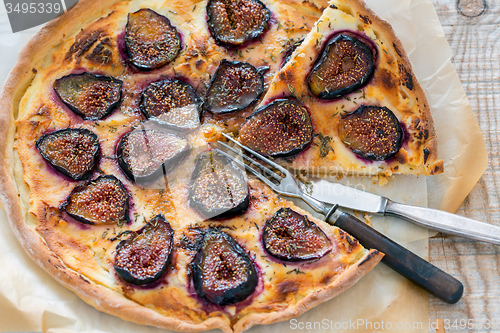 Image of Sliced pizza with figs, fork and knife.
