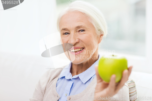 Image of happy senior woman with green apple at home