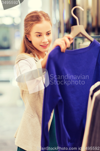 Image of happy young woman choosing clothes in mall