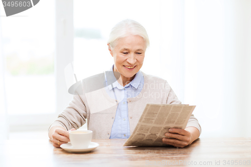 Image of senior woman with coffee reading newspaper at home