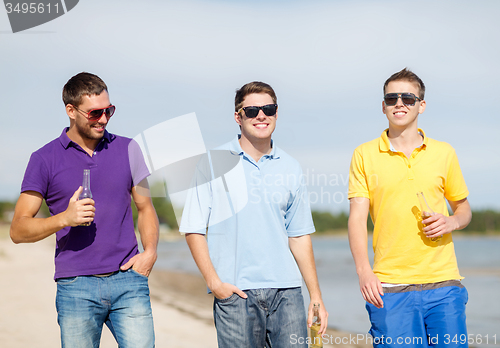 Image of happy friends drinking beer and walking on beach