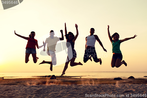 Image of smiling friends dancing and jumping on beach