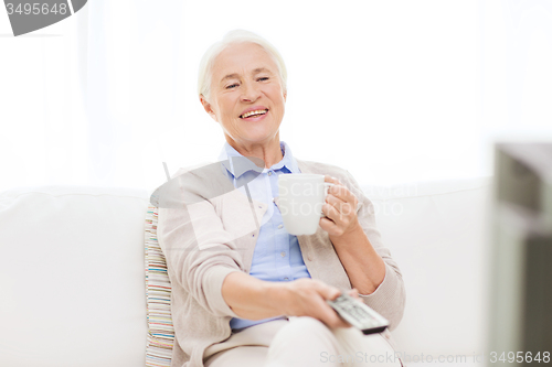 Image of senior woman watching tv and drinking tea at home