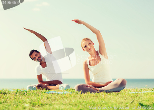 Image of smiling couple making yoga exercises outdoors