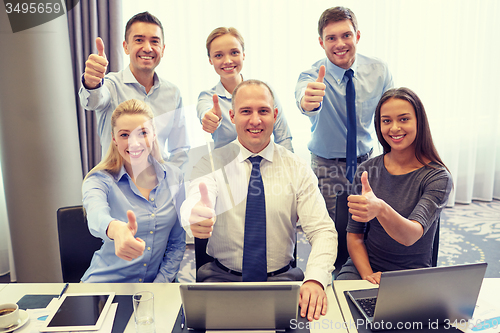 Image of business people showing thumbs up in office