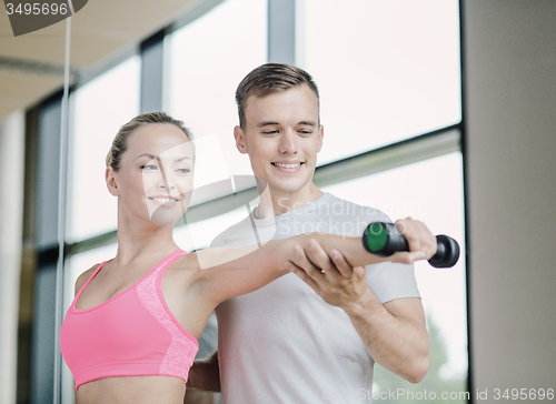 Image of smiling young woman with personal trainer in gym