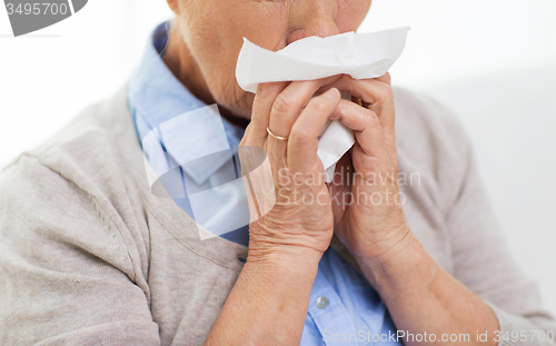 Image of sick senior woman blowing nose to paper napkin