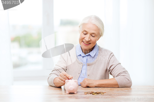 Image of senior woman putting money to piggy bank at home