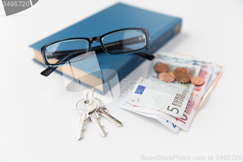 Image of close up of book, money, glasses and keys on table