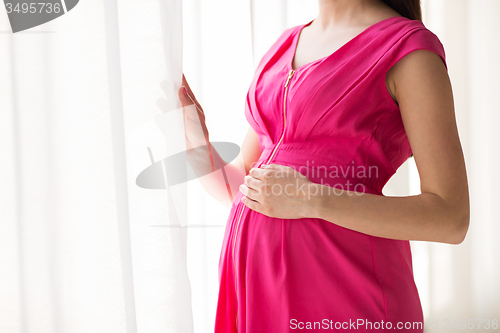 Image of pregnant woman looking through window at home