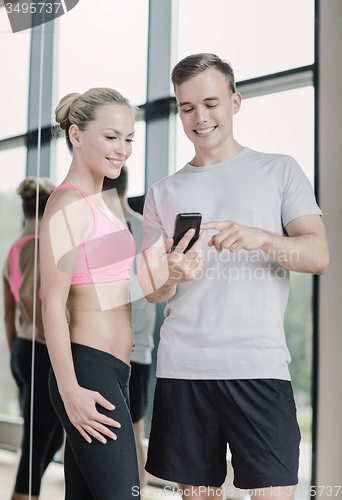 Image of smiling young woman with personal trainer in gym