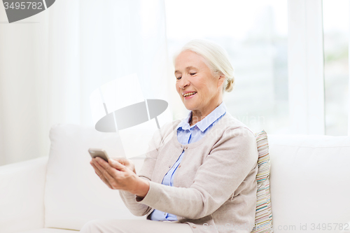 Image of senior woman with smartphone texting at home