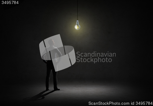 Image of businessman looking at lighting bulb in dark room