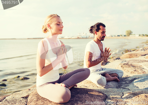 Image of smiling couple making yoga exercises outdoors