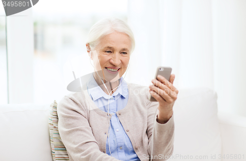 Image of senior woman with smartphone and earphones at home