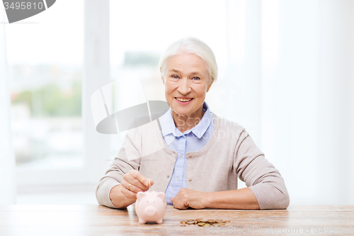 Image of senior woman putting money to piggy bank at home