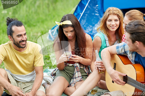 Image of happy friends with drinks and guitar at camping