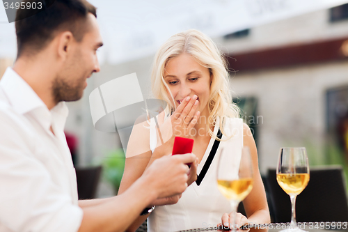 Image of happy couple with engagement ring and wine at cafe