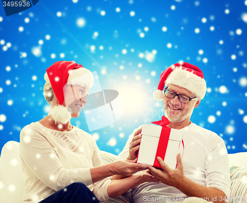 Image of happy senior couple in santa hats with gift box
