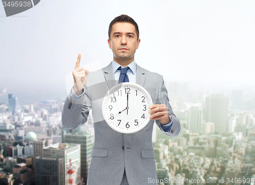 Image of businessman in suit holding clock with 8 o\'clock