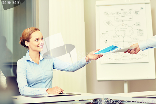 Image of businesswoman taking papers from someone in office