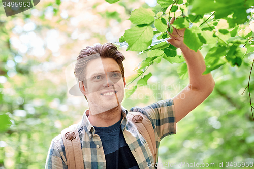 Image of smiling young man with backpack hiking in woods