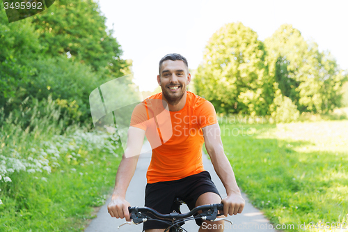 Image of happy young man riding bicycle outdoors