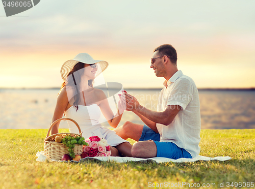 Image of smiling couple with small red gift box on picnic