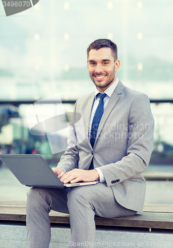 Image of smiling businessman working with laptop outdoors