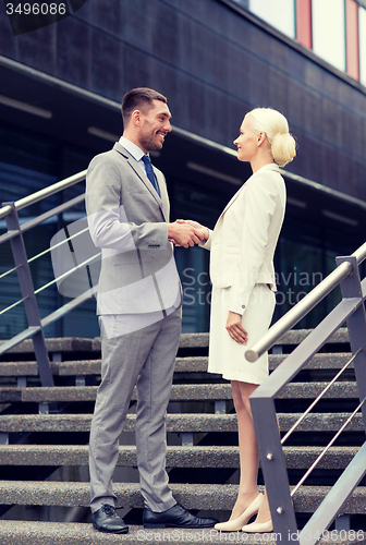 Image of smiling businessmen shaking hands on street